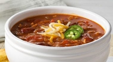 chili in a white bowl topped with cheese and jalapeno