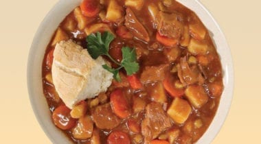 beef stew in a bowl with bread and garnish