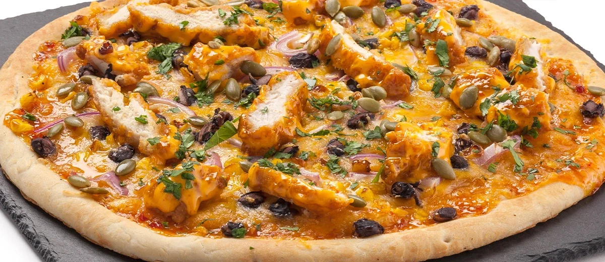 cooked pizza on a slate, toppings include chicken and orange color sauce