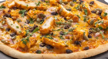 cooked pizza on a slate, toppings include chicken and orange color sauce