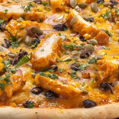 cooked pizza on a slate, toppings include chicken and orange color sauce