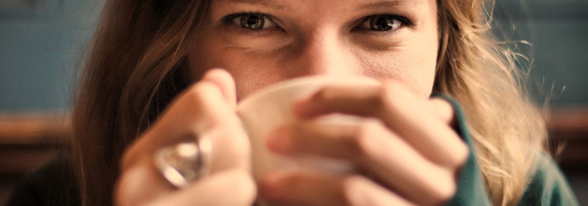 woman sipping mug, smiling with eyes