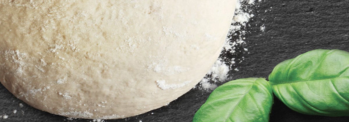 partial view of a pizza dough ball with basil leaves