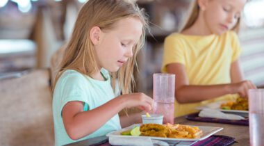 Adorable little girl on eating plate of food at table.