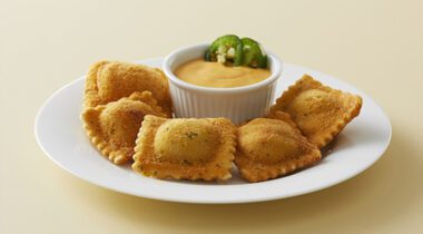 Breaded jalapeño pepper ravioli on a plate with cheese sauce and sliced jalapeños