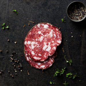 Sliced Peppered salami on dark table background surrounded by scattered spices