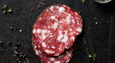 Sliced Peppered salami on dark table background surrounded by scattered spices