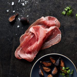 Sliced Prosciutto on dark table background surrounded by scattered spices