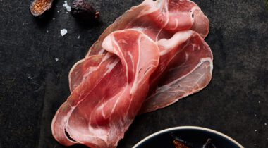 Sliced Prosciutto on dark table background surrounded by scattered spices