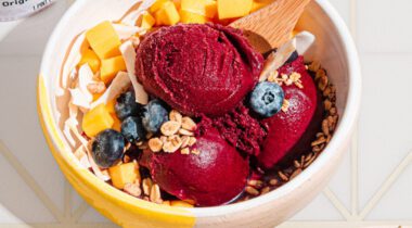 Bowl of granola coconut flakes blueberries and acai berry sorbet with wooden spoon