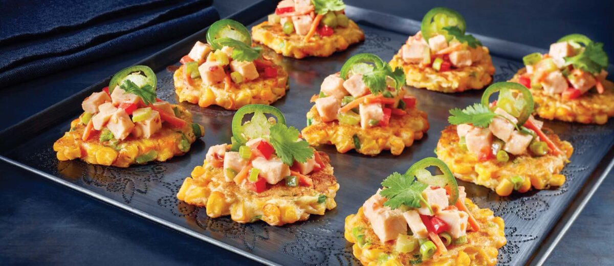 black plate of corn cake appetizers topped with turkey salad