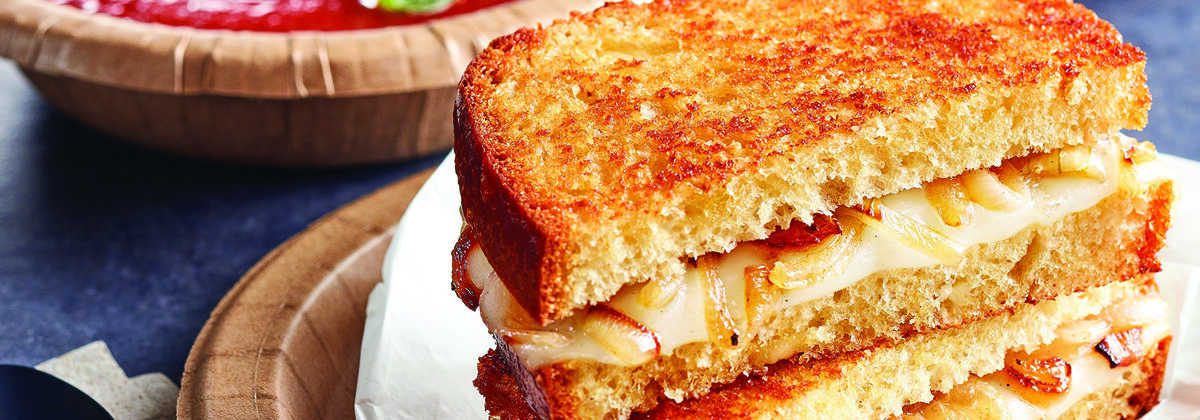 grilled cheese sandwich sliced, stacked on top of each other on plate with bowl of soup in background