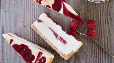 three slices of cheesecake with bowl of raspberries .