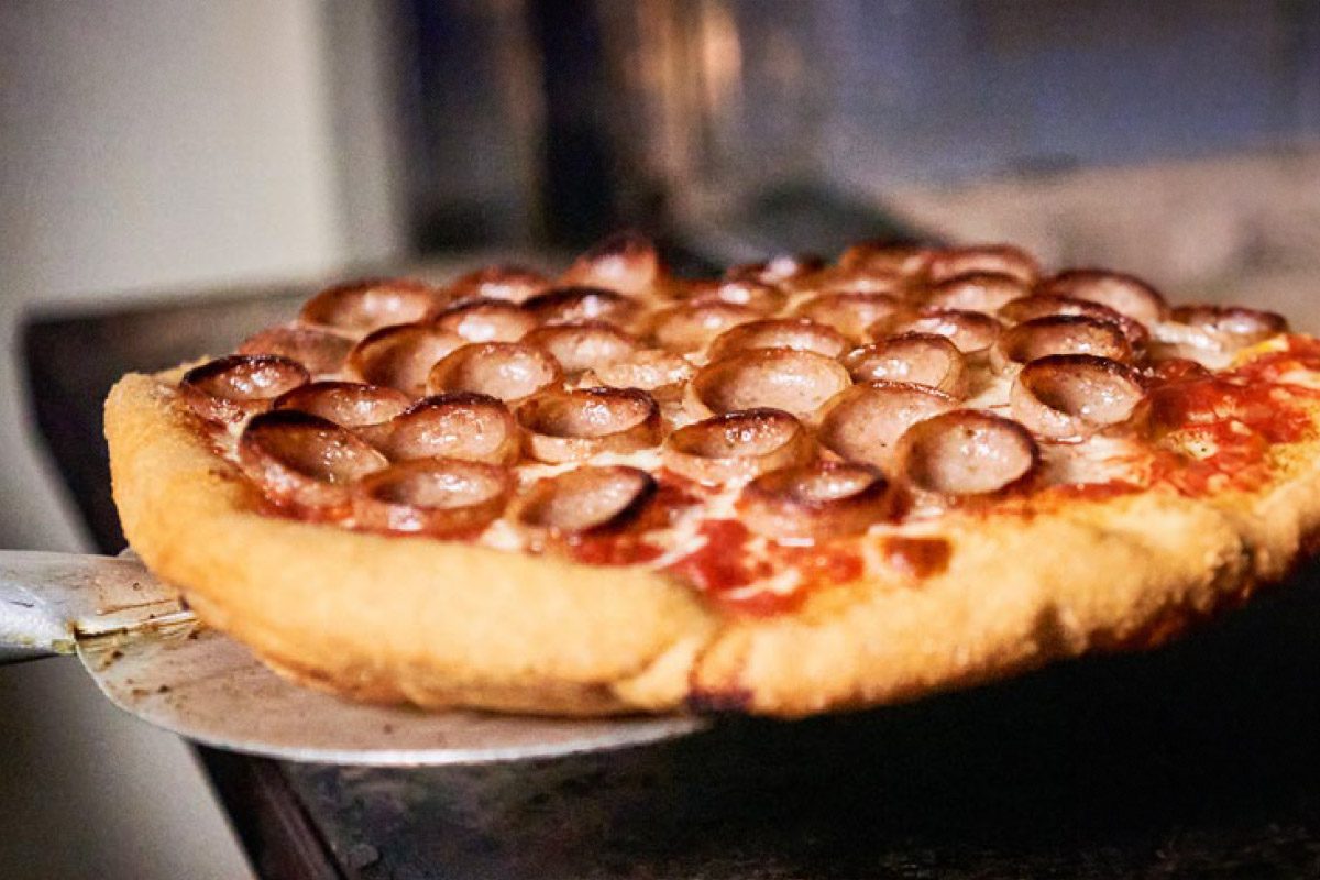 cupped sausage slices on a pizza coming out of an oven
