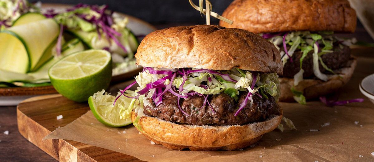 2 burgers with slaw and lime slices on cutting board