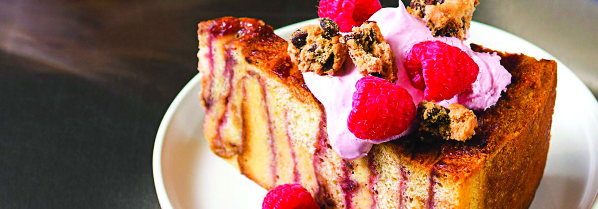 slice of raspberry bread pudding with cookie pieces and fresh raspberries on white plate