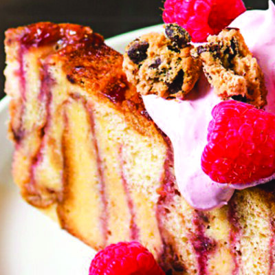 slice of raspberry bread pudding with cookie pieces and fresh raspberries on white plate