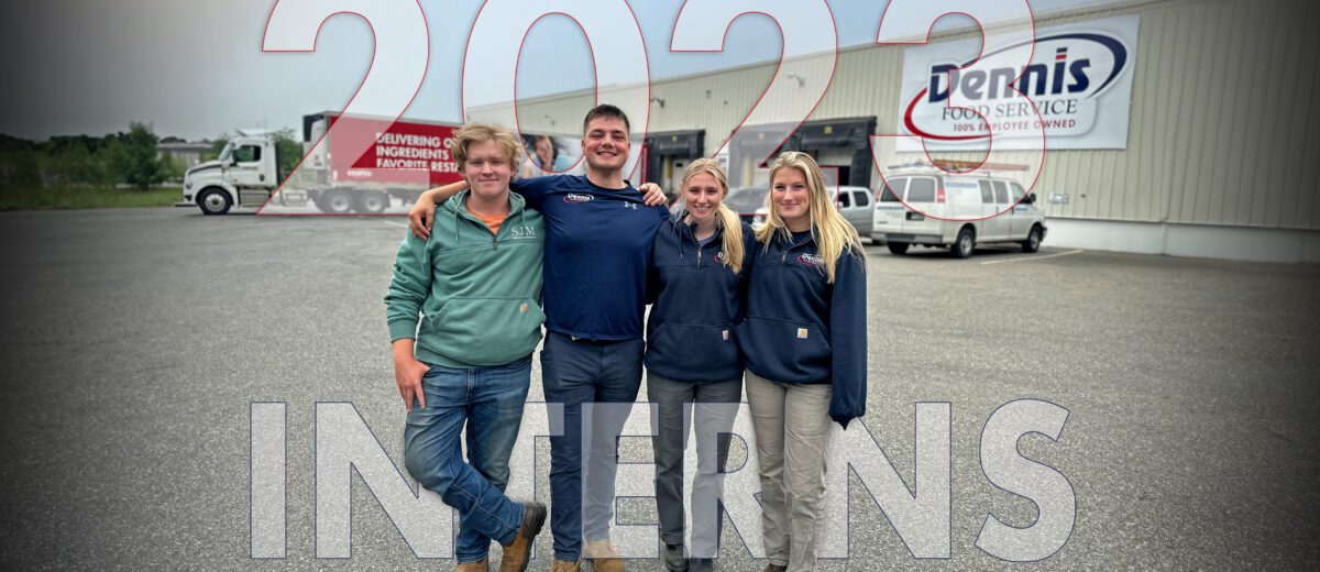 four collage students standing together outside in front of tractor trailer truck and Dennis food service building.