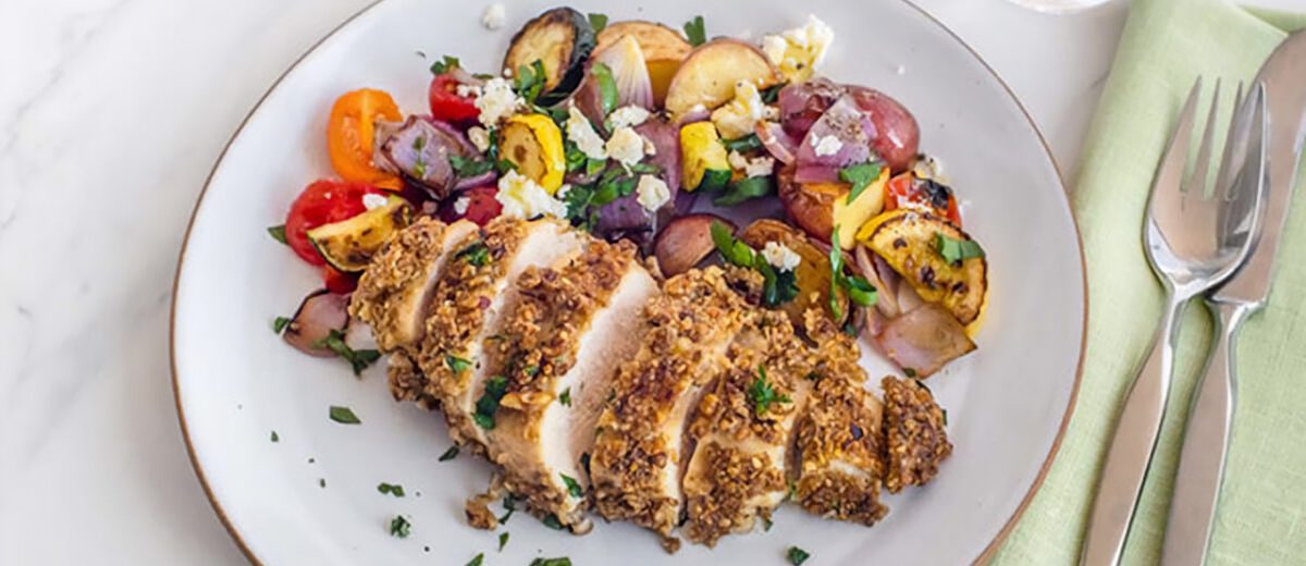 breaded sliced chicken breast on a white plate with cooked vegetables