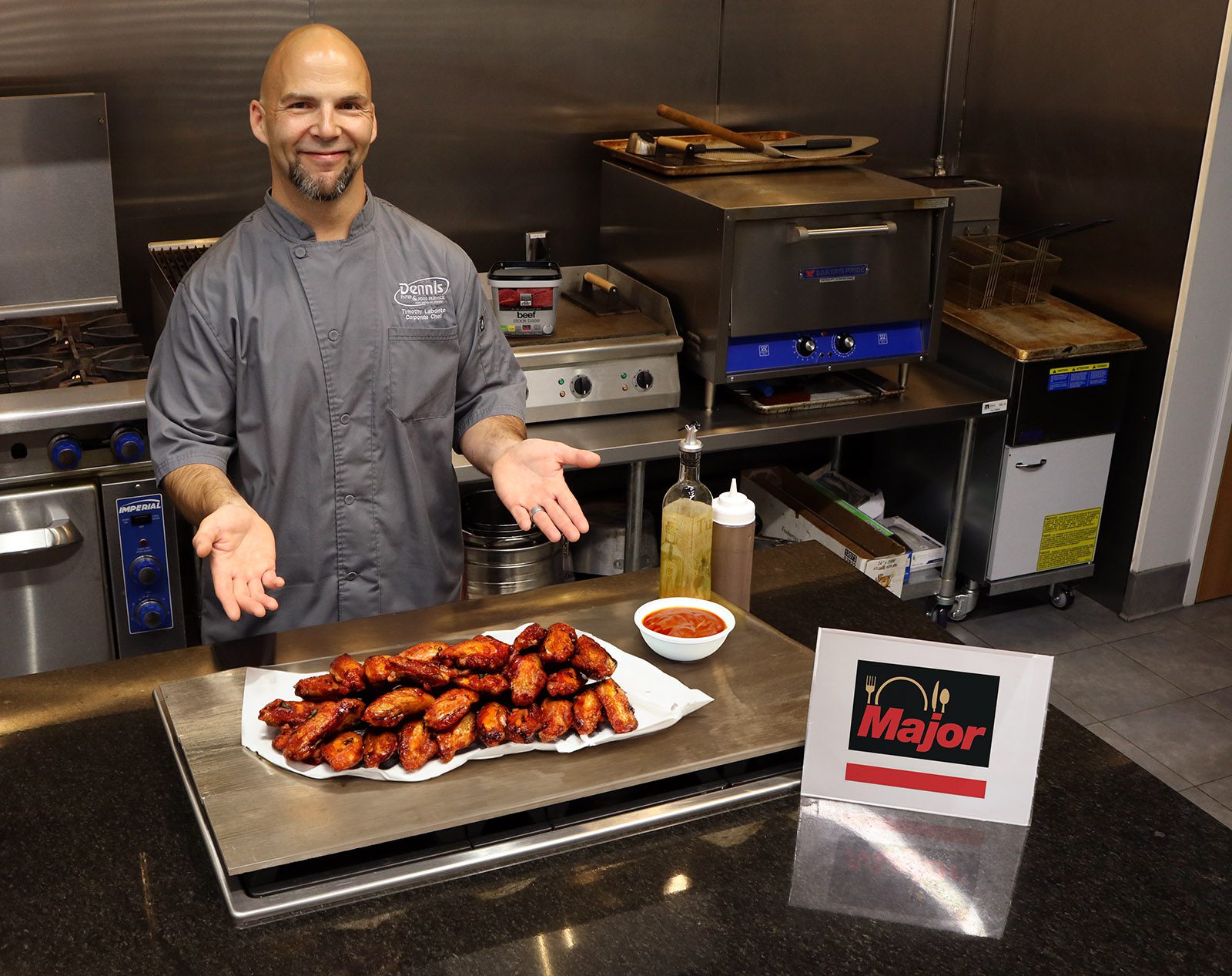 chef in a gray coat presenting platter of bbq chicken wings in a kitchen