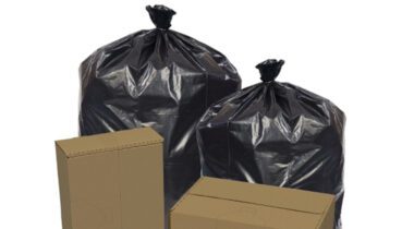 two rectangle cardboard boxes next to two large black trash bags tied up