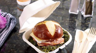 turkey sandwich on pretzel bun in opened square container on cafe tabletop