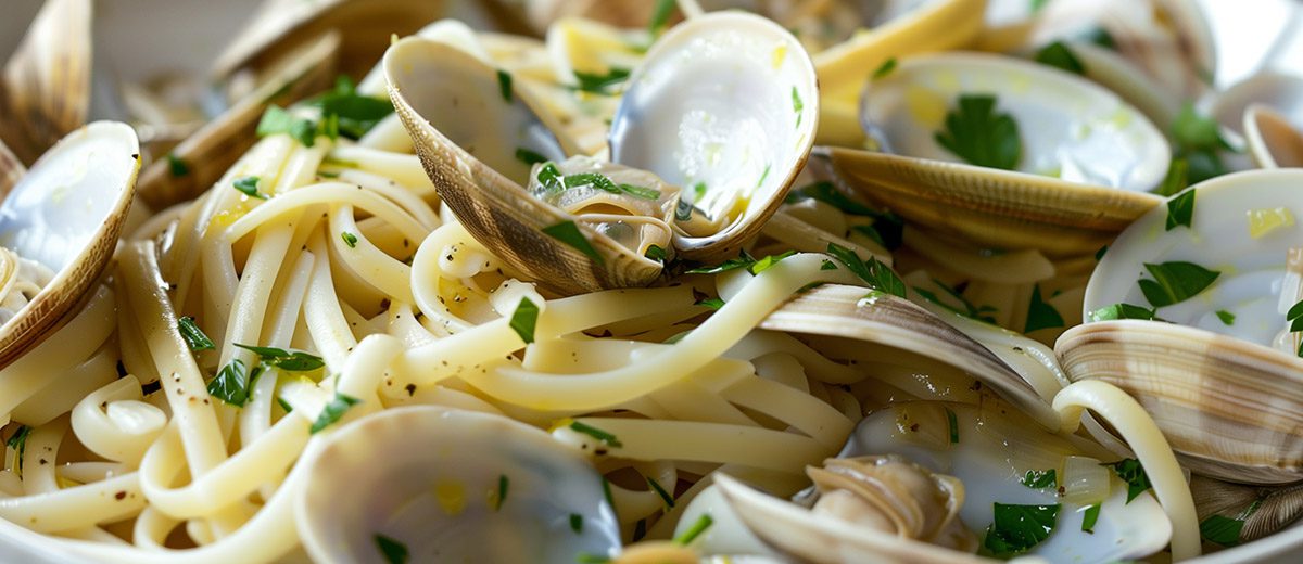 cooked clams and herbs on a plate with linguini noodles