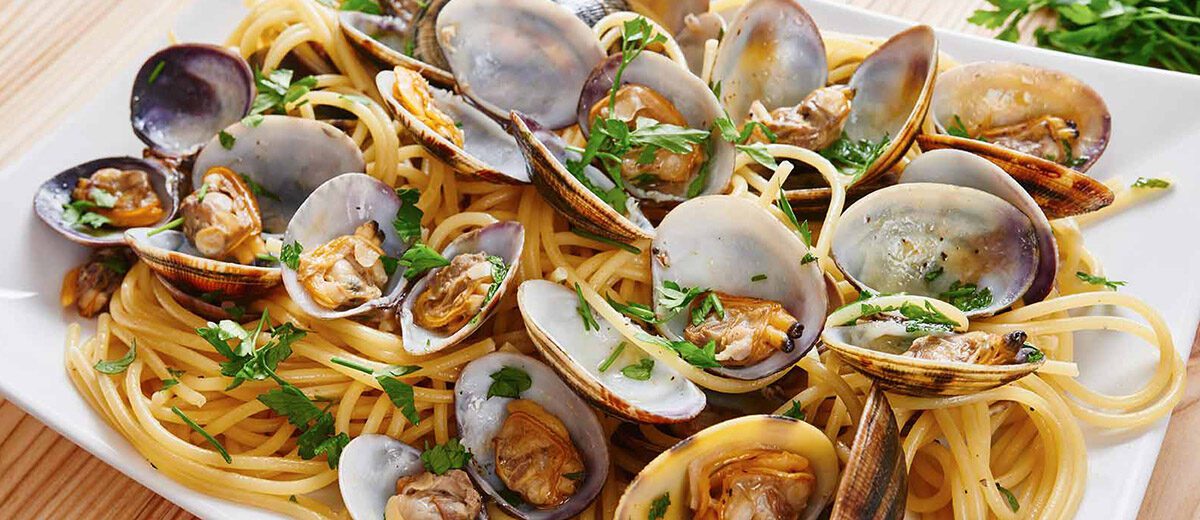 cooked clams and herbs on a plate with linguini noodles