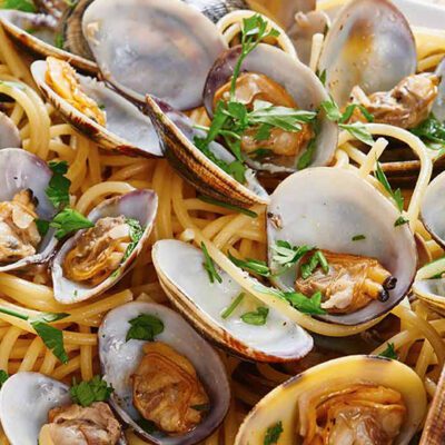 cooked clams and herbs on a plate with linguini noodles