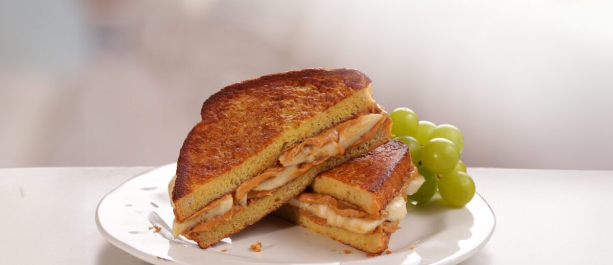 sliced peanut butter and banana sandwich on white plate with green grapes.