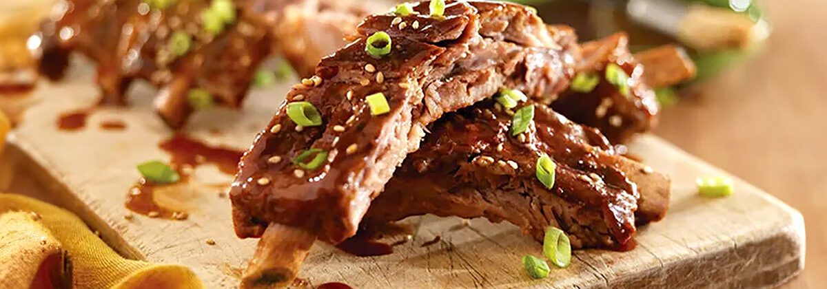 wood plate of cooked pork ribs with sauce and scallions
