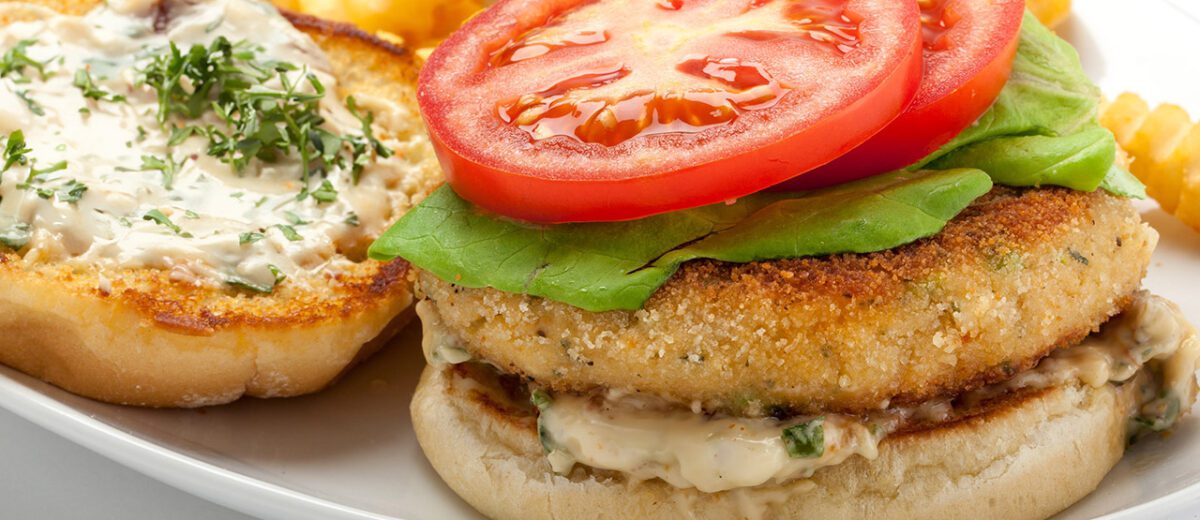 crab cake on a bun with lettuce, tomato, white sauce, herb sprinkled