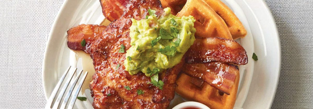 Cooked chicken breast on plate of waffles and bacon with guacamole on top