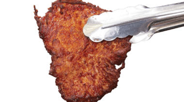 tongs holding piece of fried chicken