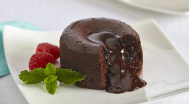 chocolate lava cake cut on white plate with mint leaf and 2 raspberries
