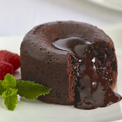 chocolate lava cake cut on white plate with mint leaf and 2 raspberries