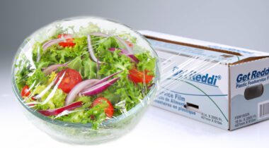 clear bowl of salad wrapped in clear film wrap and box of film wrap