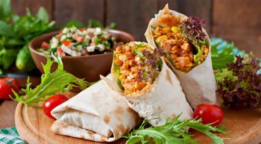 burrito wraps on a cutting board with fresh veggies