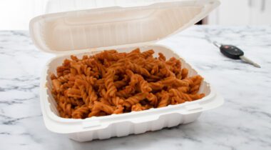 white hinged container with cooked spiral noodles on granite tabletop