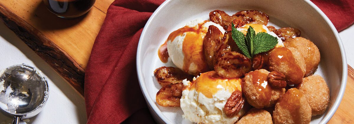 White bowl with Horchata Bites covered in caramel sauce, walnuts, bananas and ice cream