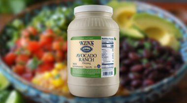 a gallon plastic jar of salad dressing in front of an out of focus salad