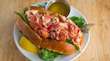 a lobster roll on a plate with butter and a lemon wedge