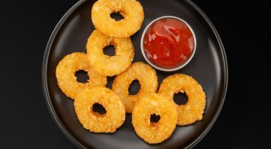 fried potato rings with a cup of ketchup on a black plate