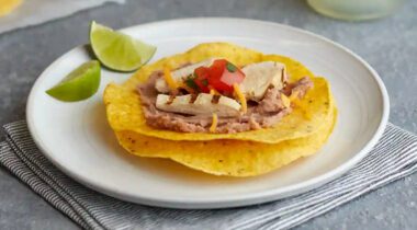 corn tortillas with chicken and refried beans on a white plate, wedge of lime