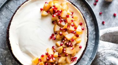 looking down on a prepared cheesecake with pears and pomogranite covering half the cheesecake