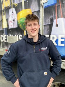 a young man stnads smiling in a blue sweatshirt in front of a truck