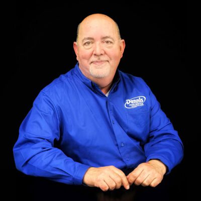 man, bald with white chin hair in blue shirt with white logo on black background