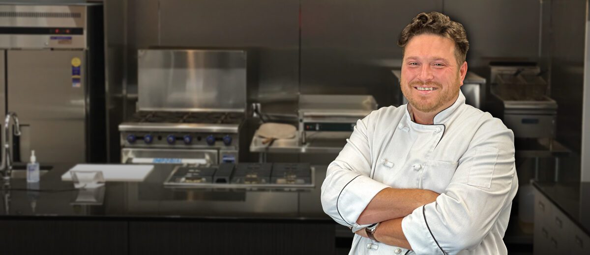 male chef standing in kitchen with arms crossed