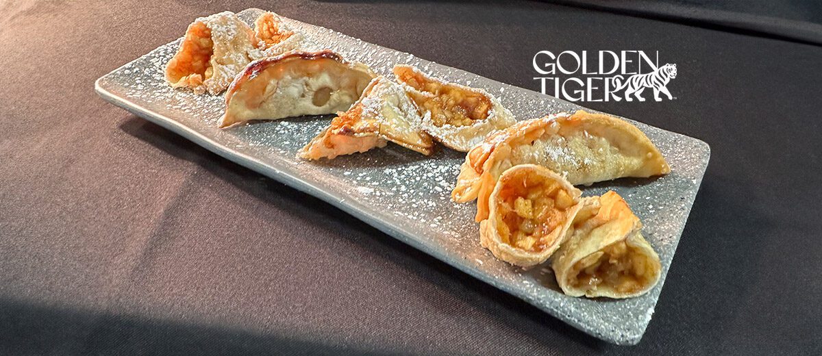 apple pie potsickers sprinkled with powdered sugar on a gray plate, on a black table cloth.