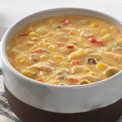 a bowl of chicken and corn chowder, spoon, crusty bread